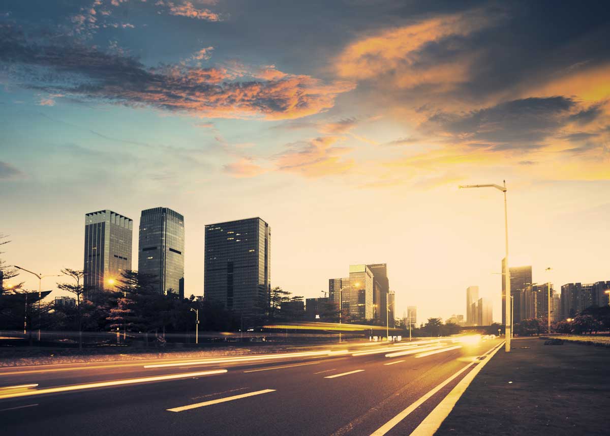 A city road at golden hour with headlights streaking towards the skyline