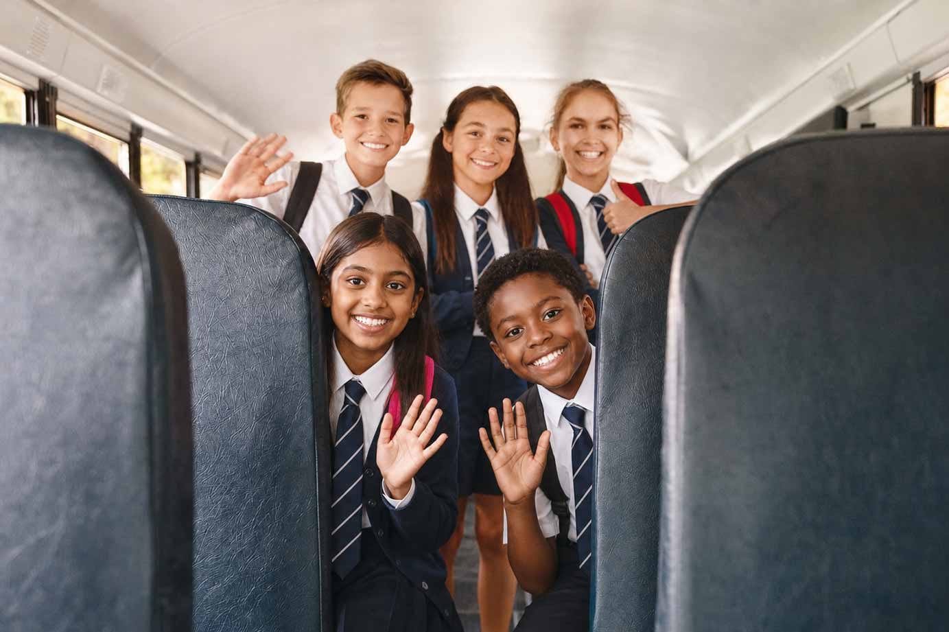 Five school learners in uniform smiling and waving on a Beremi scholar bus